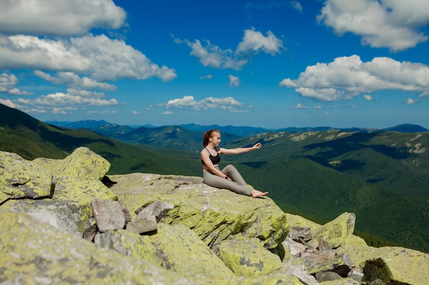 Mädchen, das Yogaübungs-Lotoshaltung an der Spitze des Berges tut.