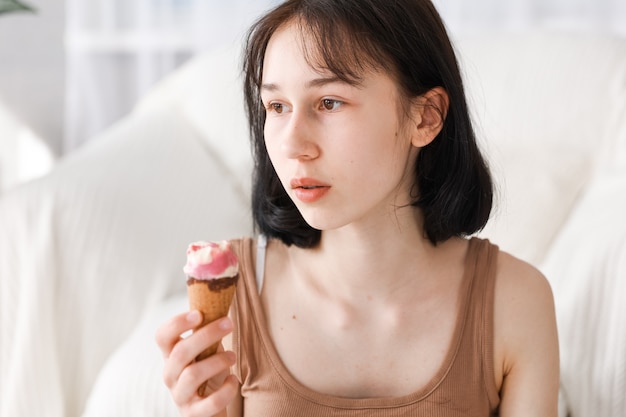 Mädchen, das zu Hause Eiscreme mit Wohnzimmerhintergrund isst. Kindermädchen genießen das Essen und das hungrige Konzept.