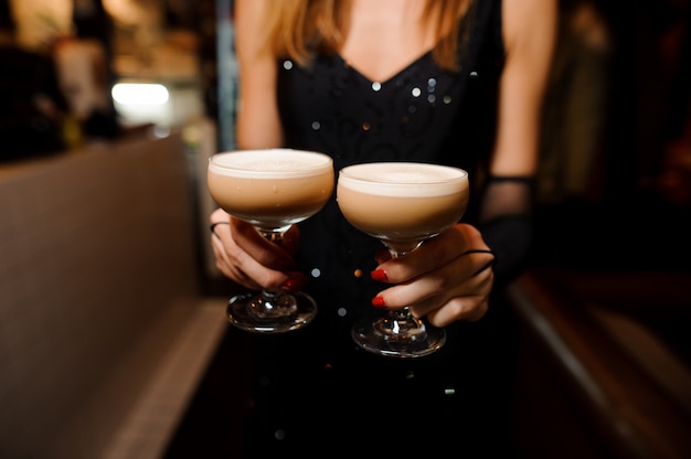 Mädchen, das zwei Gläser mit einer sauren Mischung des alkoholischen Cocktails hält
