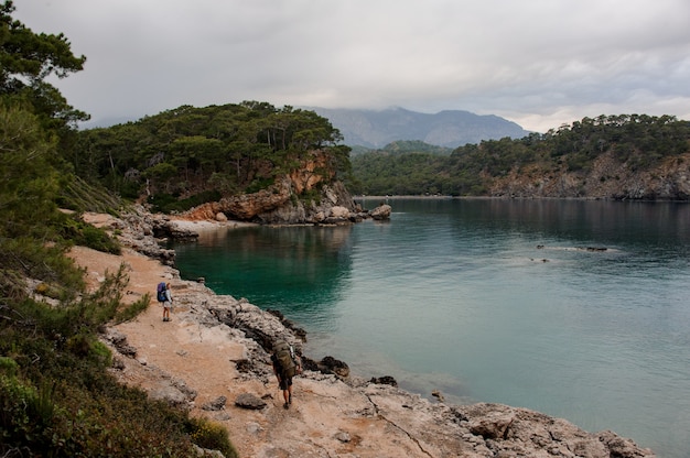 Mädchen der hinteren Ansicht mit Rucksack und Wanderstöcken gehend auf die felsige Seeküste