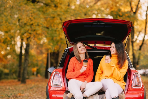 Mädchen, die im Herbstpark im Herbststimmungskonzept des roten Autos spazieren gehen