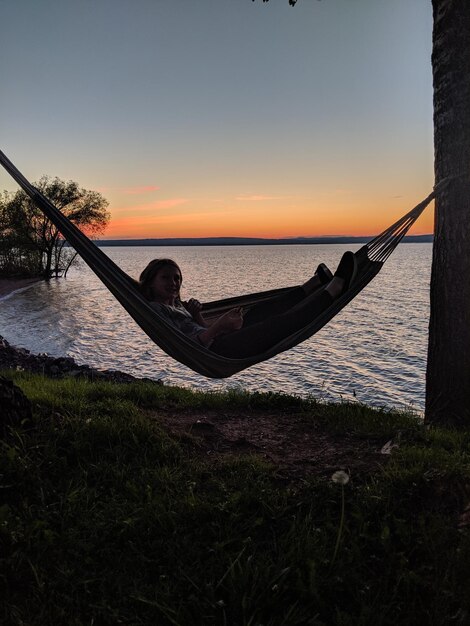Mädchen entspannt sich bei Sonnenuntergang in einer Hängematte vor Meer und Himmel