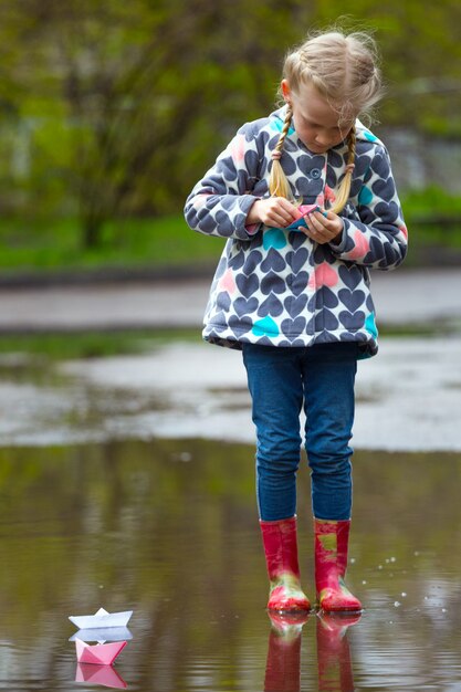 Mädchen fährt das rosa Papierboot in einer Pfütze im Regen, Frühling