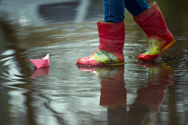 Mädchen fährt das rosa Papierboot in einer Pfütze im Regen, Frühling