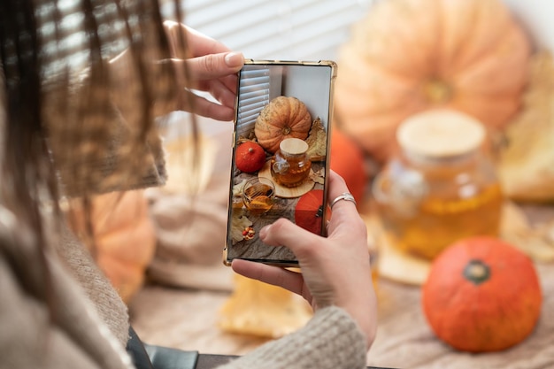 Mädchen fotografieren Kürbisse Blätter im Herbst und Teekanne auf einem Fenster Mädchen fotografieren am Telefon rustikale Halloween-Zusammensetzung Happy Thanksgiving und Halloween