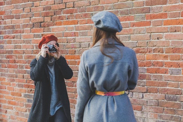 Mädchen fotografiert ihre Freundin vor der Backsteinmauer im städtischen Straßenfotografen und in der Jugend