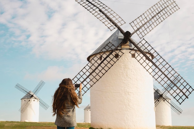 Mädchen fotografiert mit ihrem Handy eine traditionelle Windmühle mit grüner Jacke