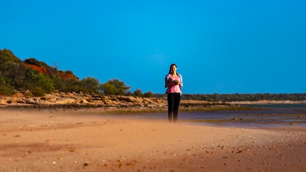 Mädchen geht am roten Sandstrand mit roten Klippen im Hintergrund, Terra Rosa in Australien