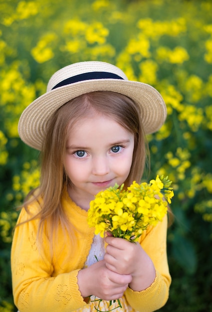 Mädchen geht durch das Feld und sammelt Blumen, schönes Lächeln, Rapsfeld, trägt einen Hut