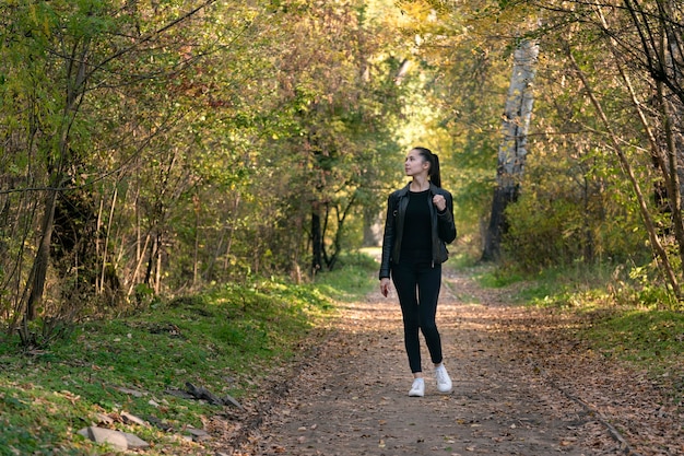 Mädchen geht in den Herbstpark. Junge schöne Frau in schwarzer Kleidung im Wald. Gasse, Promenade.