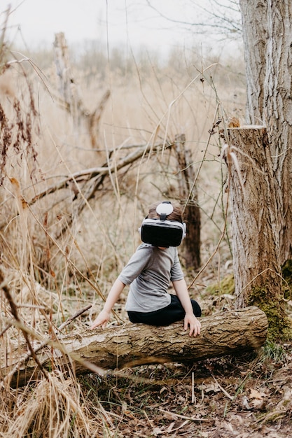 Mädchen genießen virtuelle Realität, die auf Baum im Freiluftpark sitzt. VR-Headset-Brillengerät. Menschen- und Technologiekonzept