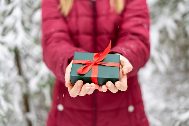 Mädchen gesichtslos in Händen halten Geschenk grüne Box mit rotem Band gegen schneebedeckten Baum Weihnachten Neujahr