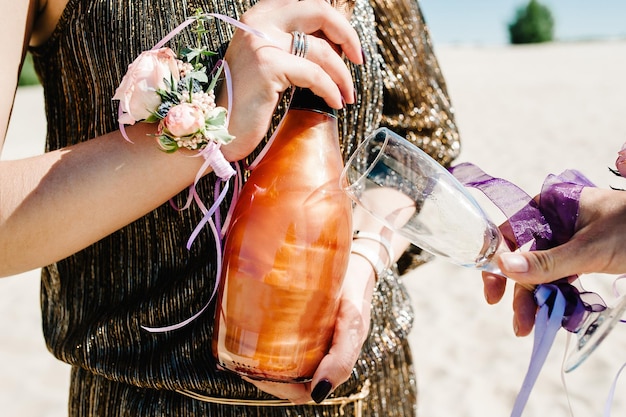 Mädchen hält Champagner und Glas Glashand mit Bändern Blumen dekoriert Party im Stil Boho Jungfernabend Junggesellinnenabschiede Junggesellinnenabschied Nahaufnahme