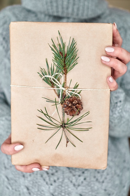 Mädchen hält ein Buch für ein Geschenk, das in Bastelpapier eingewickelt ist, verziert mit einem Tannenzweig mit einem Kegel