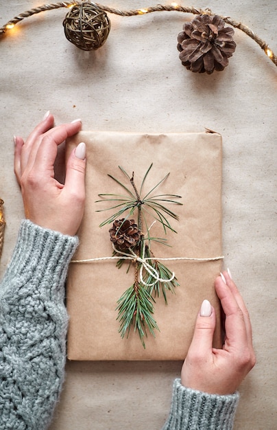 Mädchen hält ein Buch für ein Geschenk, das in Bastelpapier eingewickelt ist, verziert mit einem Tannenzweig mit einem Kegel