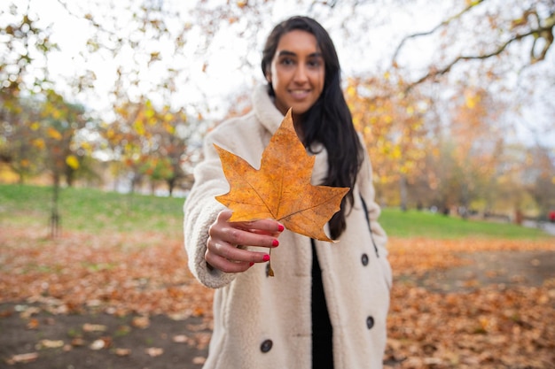 Mädchen hält ein orangefarbenes Blatt, das gerade vom Baum in einem öffentlichen Park gefallen ist Herbstkonzept