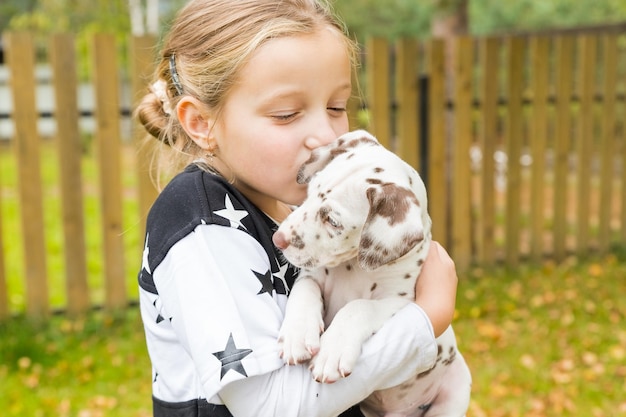 Mädchen hält einen Welpen auf ihren Armen. Nettes kleines Mädchen, das Dalmatiner-Welpen umarmt. Kleines Mädchen mit blonden Haaren