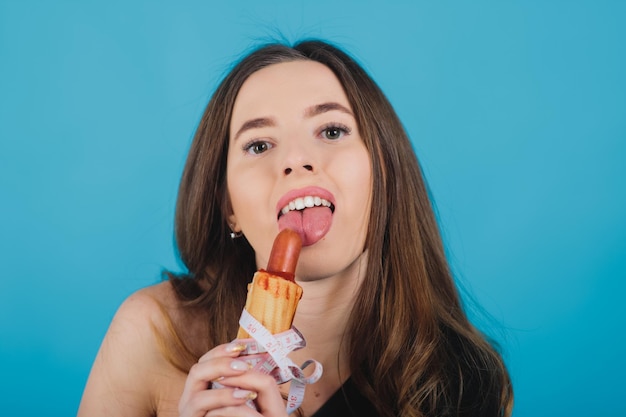 Mädchen hält Hot Dog in der Hand mit Maßband auf blauem Hintergrund