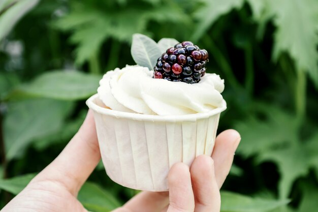 Mädchen hält in den Handkleinen kuchen mit Schlagsahne und Brombeere. Lebensmittelminimalismus auf grünem Hintergrund.