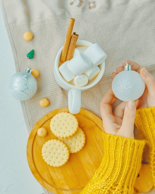 Mädchen hält Weihnachtskugel in der Hand Tasse Kakao mit Marshmallows und Zimtplätzchen auf einem Tablett ...