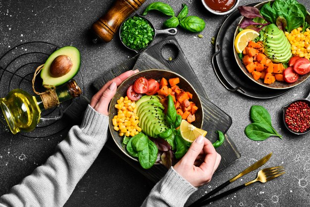 Mädchen halten eine Schüssel mit einem vegetarischen Frühstück, Kürbis, Avocado, Mais und Tomaten in der Hand.