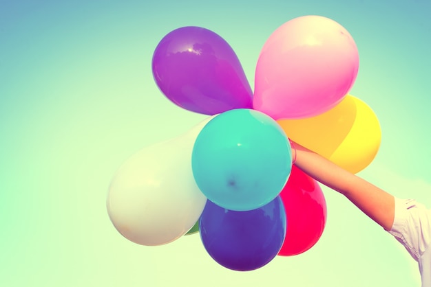 Mädchen Hand hält multi farbigen Ballons mit einem Retro-Vintage-Instagram-Filter-Effekt, Konzept der glücklichen Geburt Tag im Sommer und Hochzeit Flitterwochen Party (Vintage Farbton)