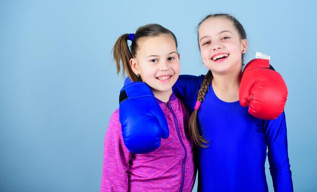 Mädchen im Boxsport Boxer-Kinder in Boxhandschuhen Selbstbewusste Teenager Boxerinnen Boxen bieten strenge Disziplin Girls niedliche Boxer auf blauem Hintergrund Konkurrenten am Ring und Freunde im Leben