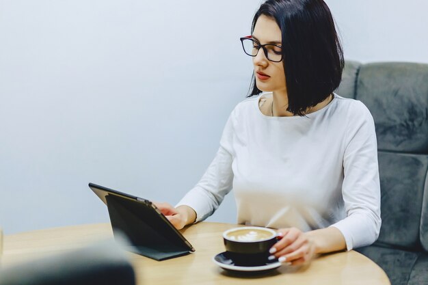 Mädchen im Café trinkt Kaffee und arbeitet an Tablette