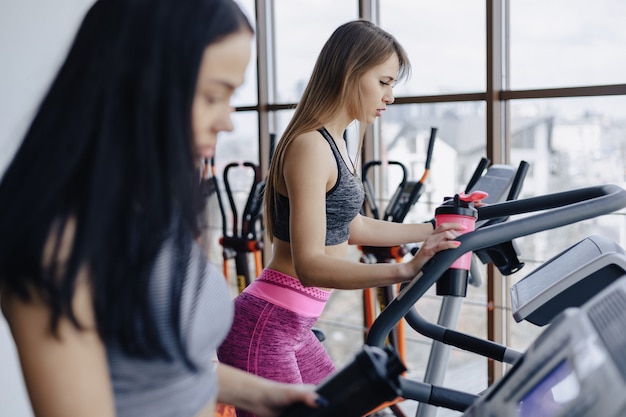 Mädchen im Fitnessstudio werden auf Laufbändern trainiert und trinken lächelnd Wasser