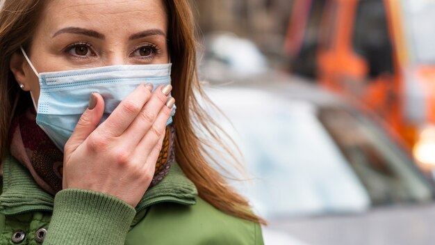 Mädchen im freien, das ihre medizinische maske mit schmutziger hand hält