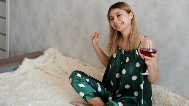 Mädchen im grünen Pyjama im Bett mit einem Glas Rotwein. Morgenwein im Bett