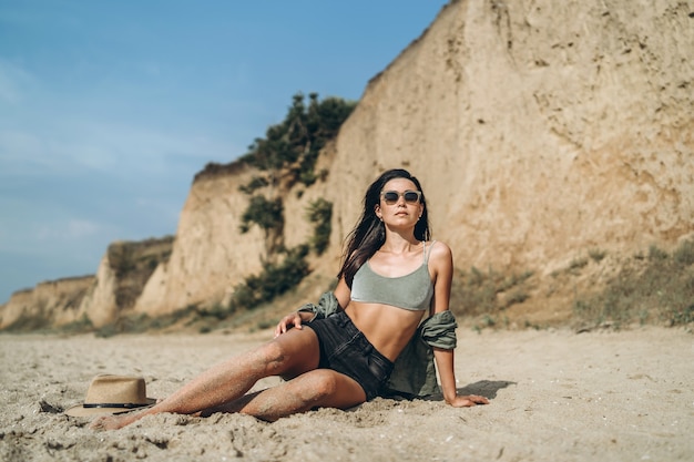 Mädchen im Hut, das am Strand mit Felsen auf Hintergrund entspannt