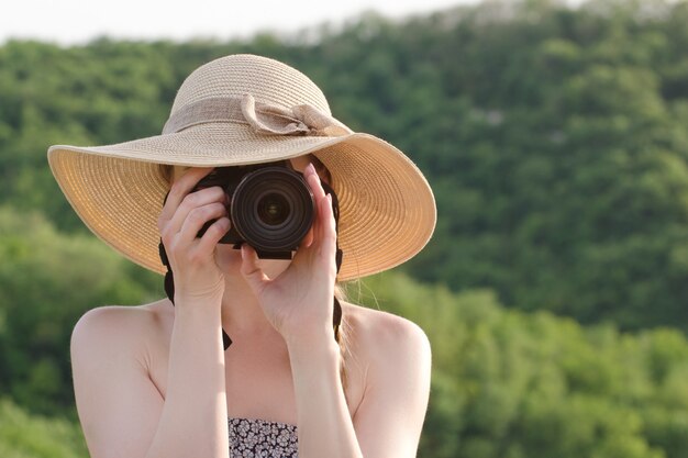 Mädchen im Hut macht Bilder vor dem Hintergrund des grünen Waldes