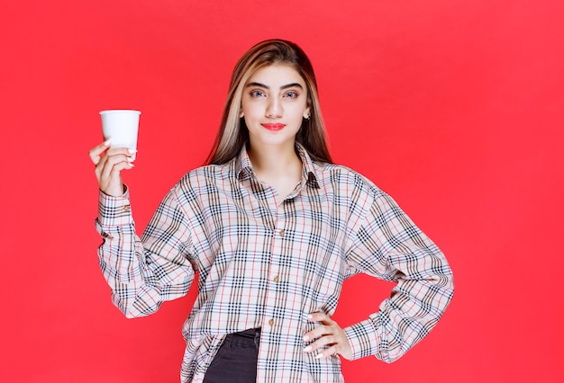 Mädchen im karierten Hemd mit einer weißen Einweg-Kaffeetasse