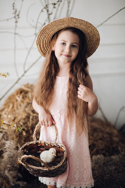 Foto mädchen im kleid und im heuhut, der korb mit kleinem küken hält