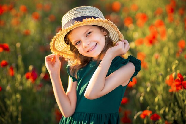 Mädchen im Kleid und im Strohhut im Freien am Mohnfeld auf Sonnenuntergang