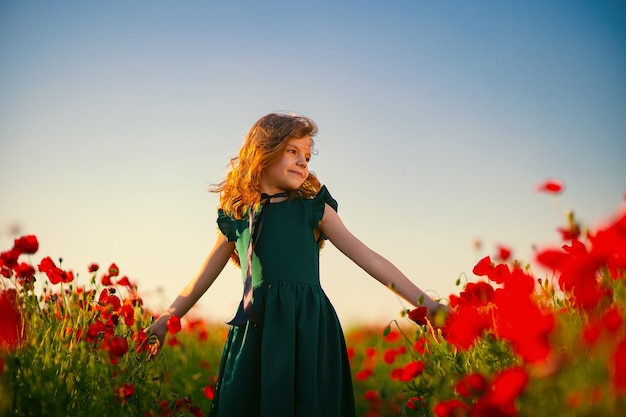 Mädchen im Kleid und im Strohhut im Freien am Mohnfeld