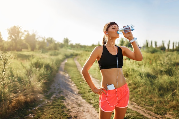 Mädchen im Kopfhörertrinkwasser nach dem Joggen