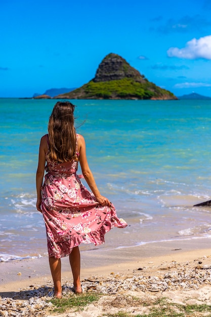 Mädchen im langen Kleid geht entlang der Küste im Kualoa Regional Park auf Oahu, Hawaii, mit Blick auf Mokolii