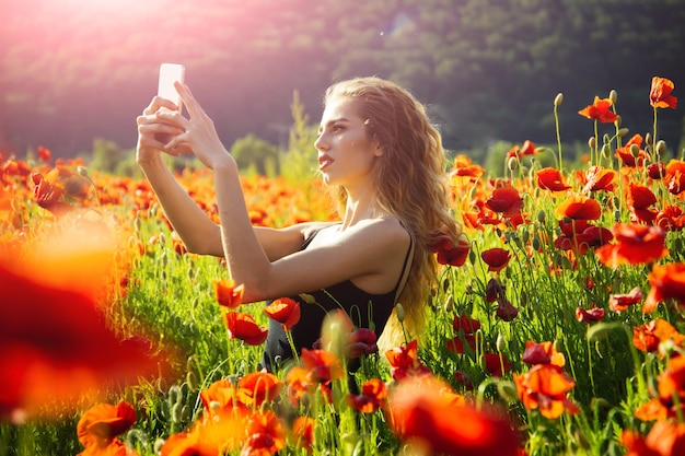 Mädchen im Mohnfeld, das Selfie-Foto mit Telefon macht