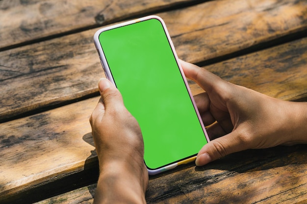 Mädchen im Park, das ein Smartphone mit Green-Screen-App auf dem Bildschirm hält Rustikaler Holztisch Chroma Key