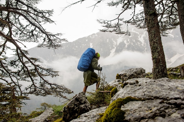 Mädchen im Regenmantel gehend auf die Felsen mit blauem Wanderrucksack und Stöcken