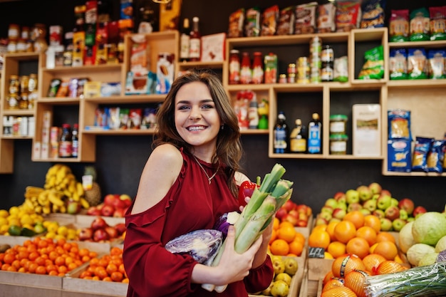 Mädchen im Rot, das verschiedenes Gemüse auf Obstspeicher hält