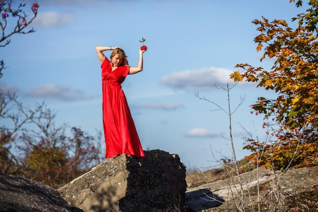 Mädchen im roten Kleid auf Felsen oder Beton zerstörte Struktur mit Eberesche auf Herbsthintergrund