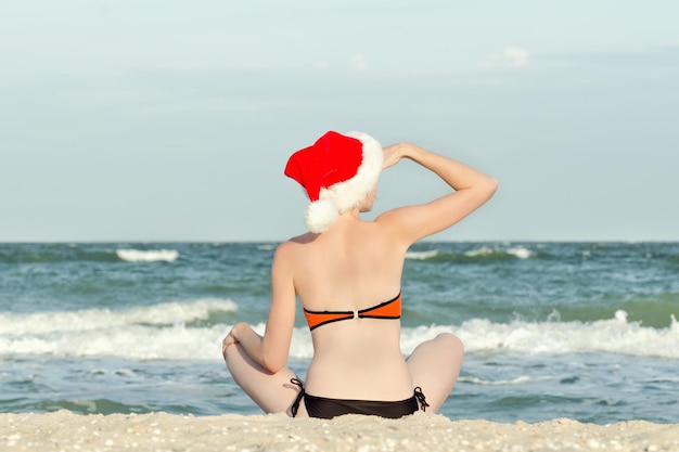 Mädchen im Sankt-Hut, der auf dem Strand sitzt Rückansicht