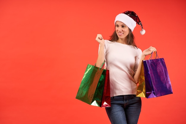 Mädchen im Weihnachtsmann-Hut mit Weihnachtseinkaufstaschen auf orangem Hintergrund