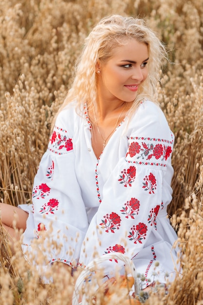 Mädchen im weißen bestickten Kleid sitzt auf dem Feld