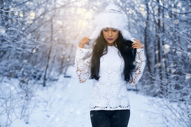 Mädchen im weißen Hut und in der weißen Bluse im Winterwald.