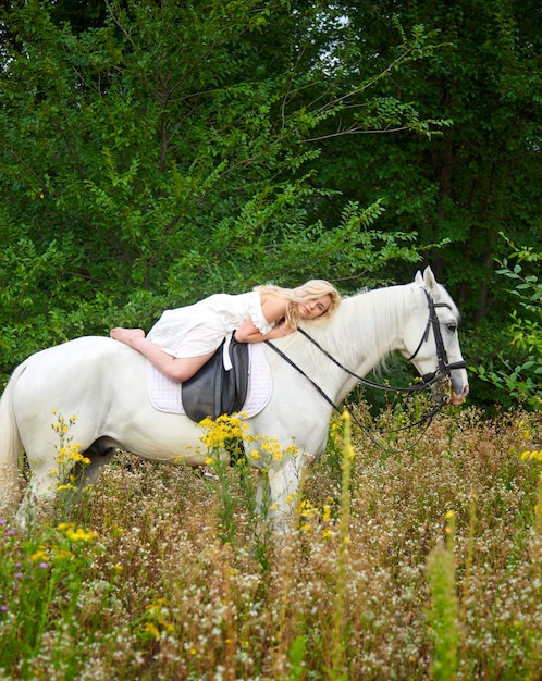 Mädchen im weißen Kleid, das ein Pferd auf dem Gebiet reitet