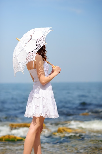 Mädchen im weißen Kleid mit Regenschirm am Strand